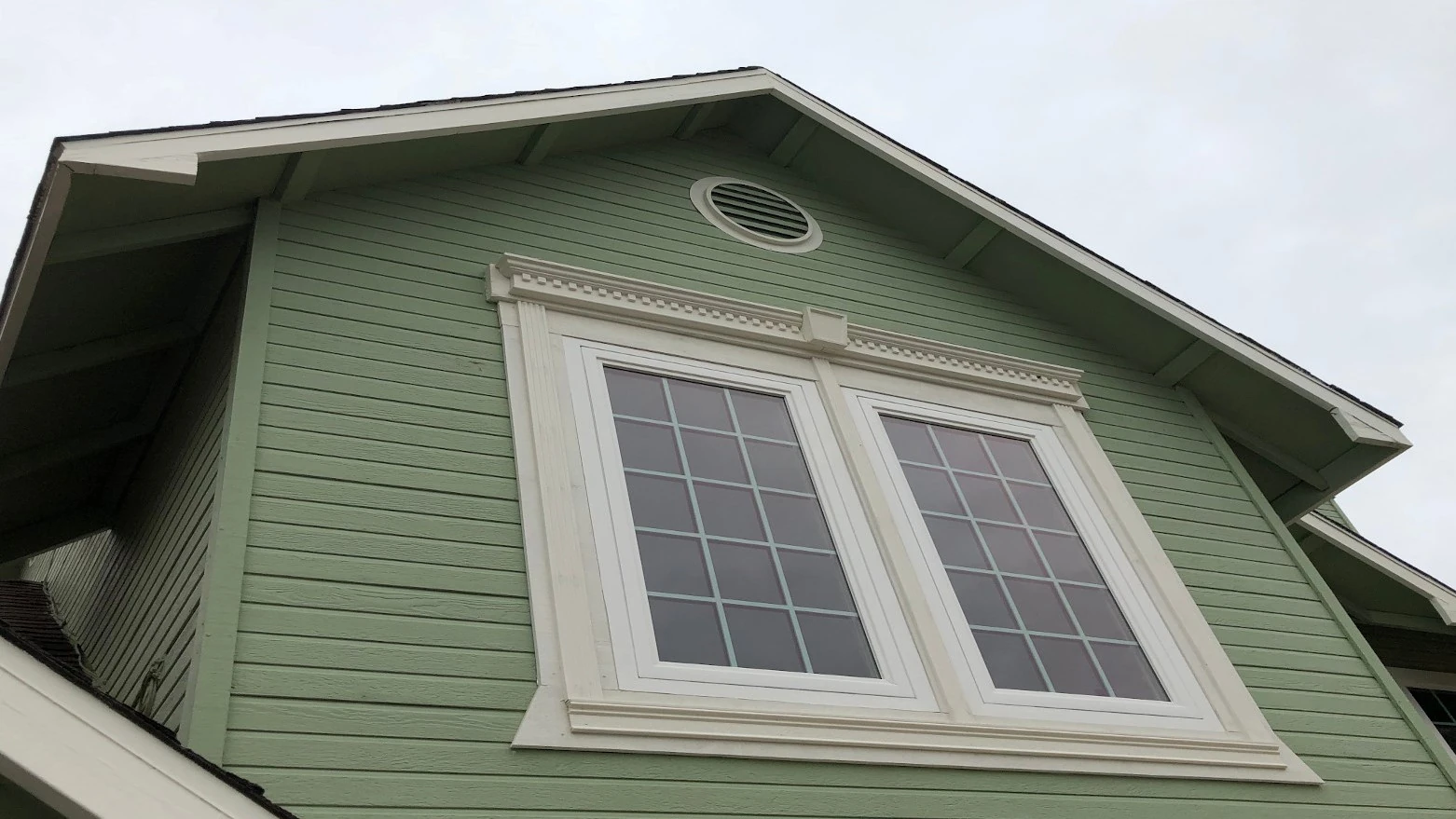 Upper part of a green house with white-trimmed double windows and a round vent above.