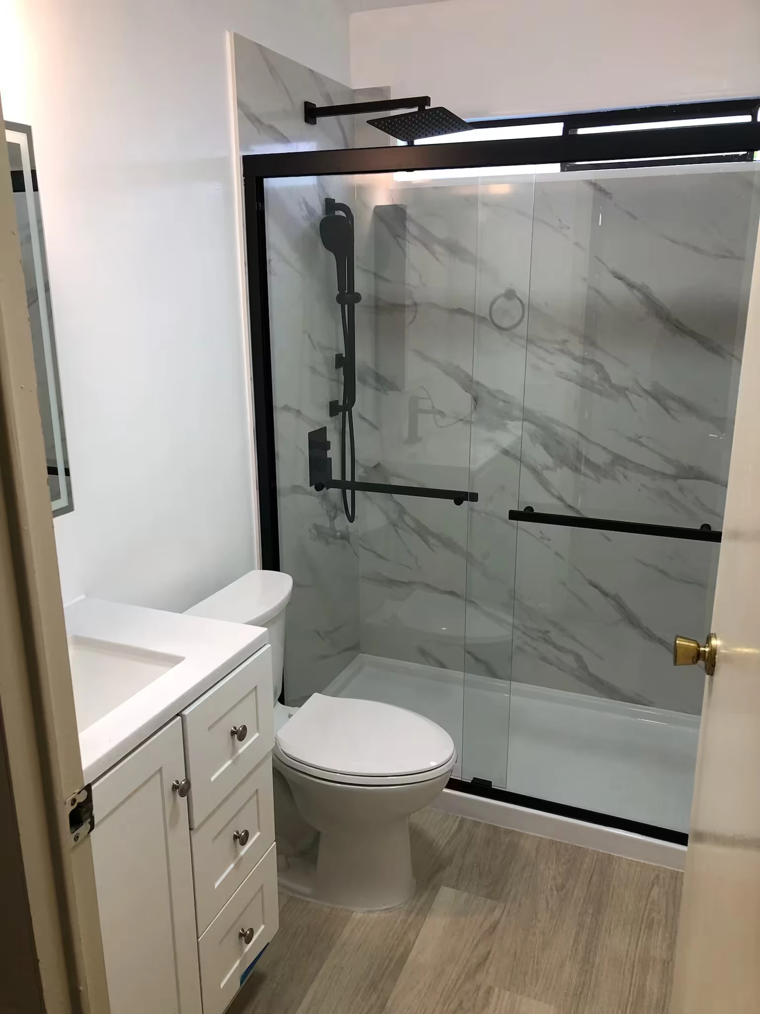 Small bathroom with a white vanity, toilet, and shower enclosure featuring black frame and gray marble-patterned walls.