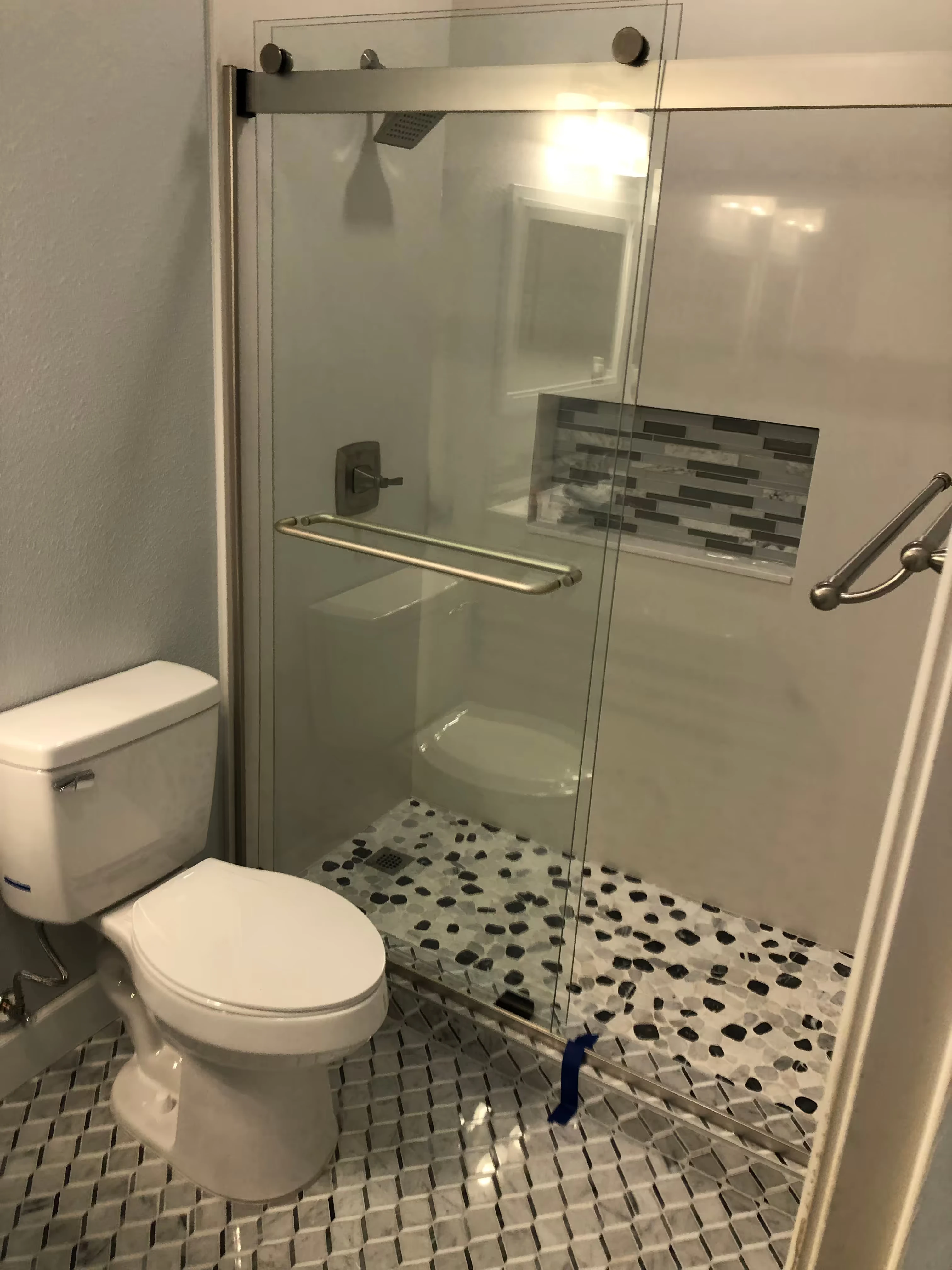 Modern small bathroom with white vanity, toilet, and glass-enclosed marble-patterned shower with black fixtures.